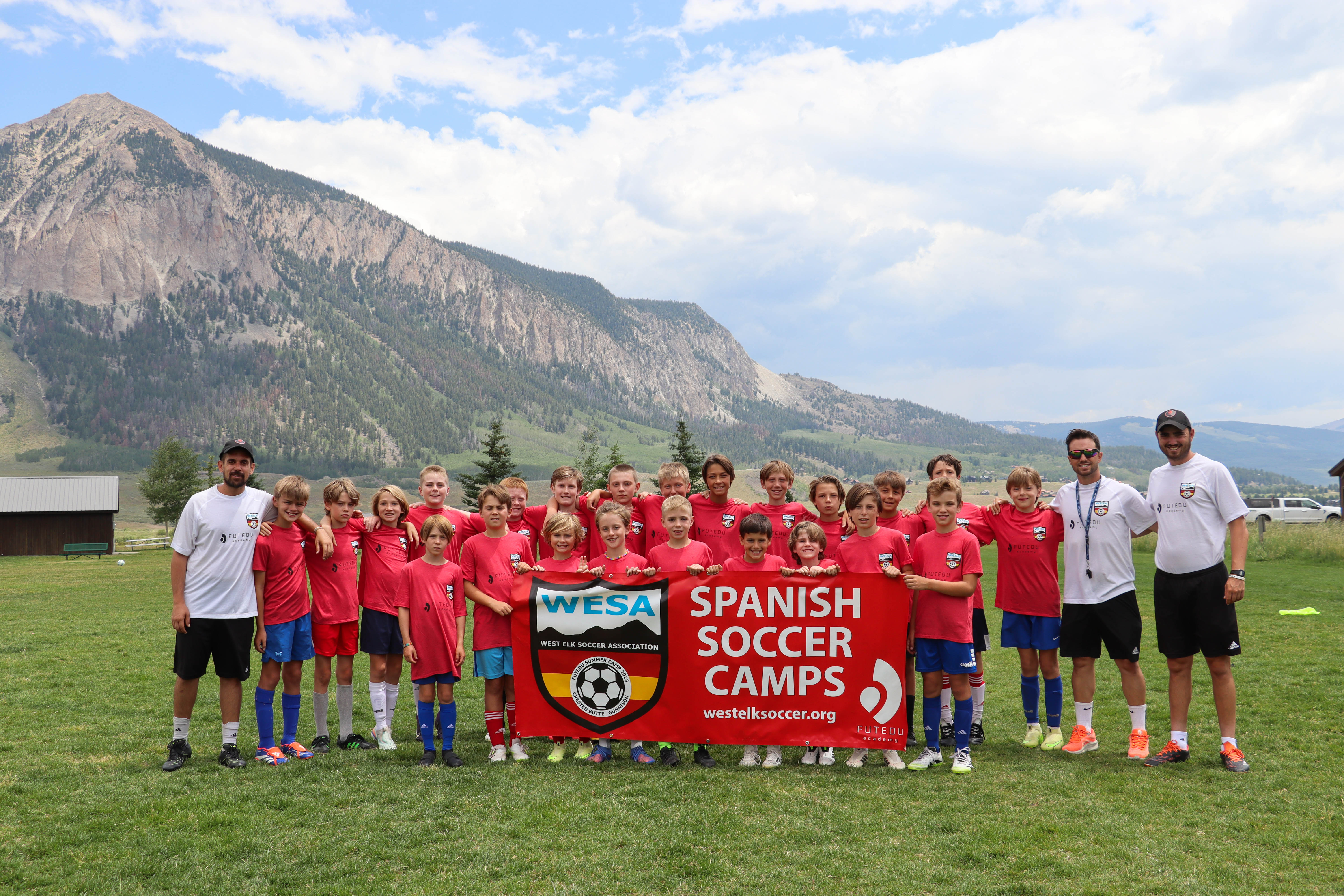 Youth players and FUTEDU Academy coaches hold a Spanish Soccer Camps banner at a summer camp in Colorado's mountains