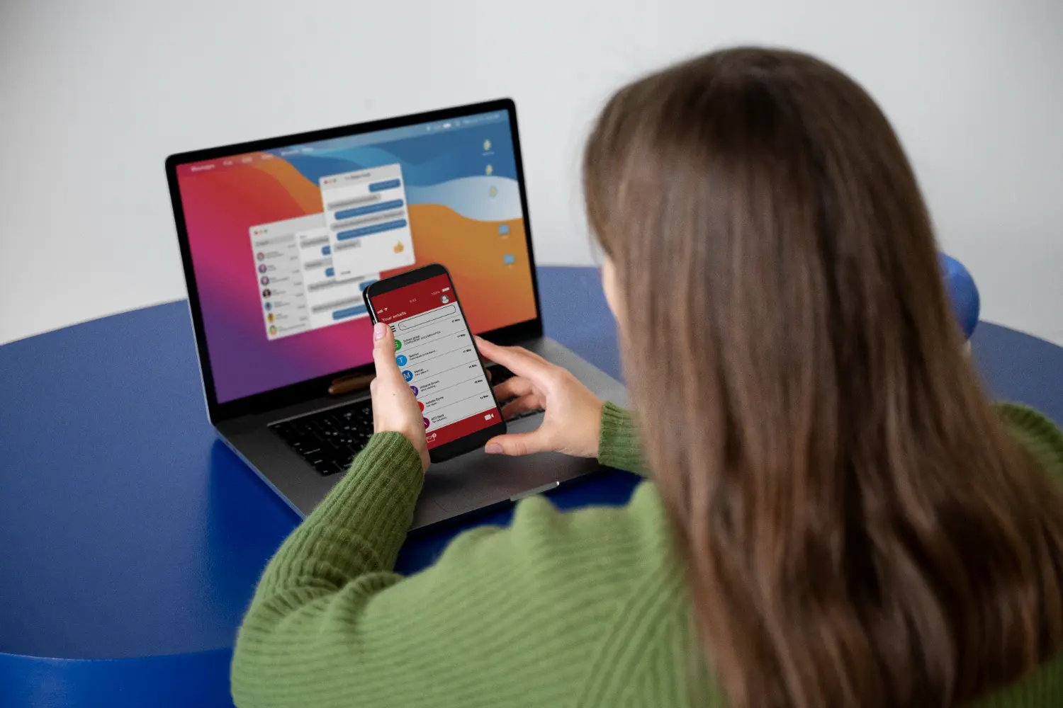 A woman checks her calendar on her laptop while using her phone for additional information.